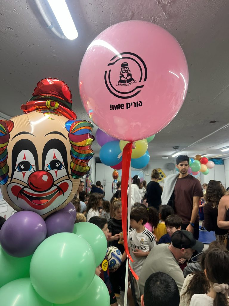 דמות ליצן בלונים ובלון פורים עם סמל עיריית רמת השרון באירוע מקלטים ונהנים