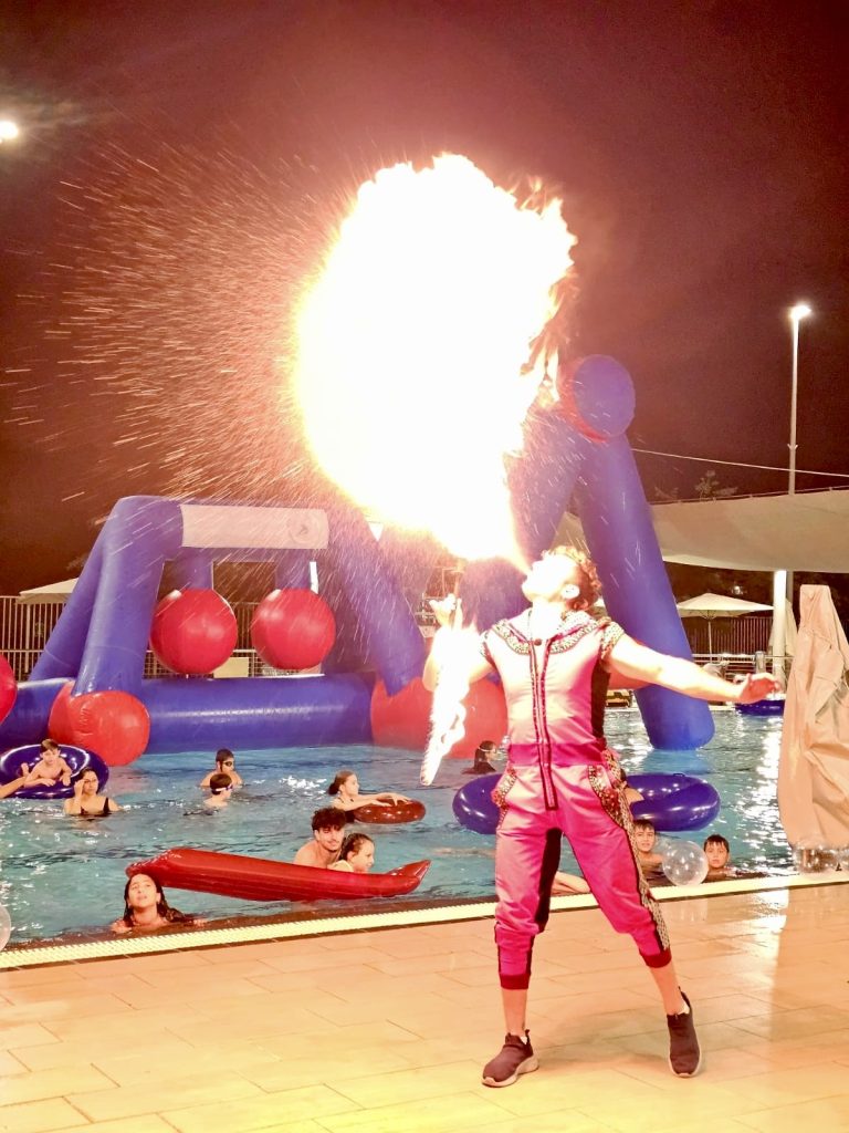 אמן אש מבצע מופע אש לצד בריכה מוקפת מתקנים מתנפחים באירוע פאנאיה