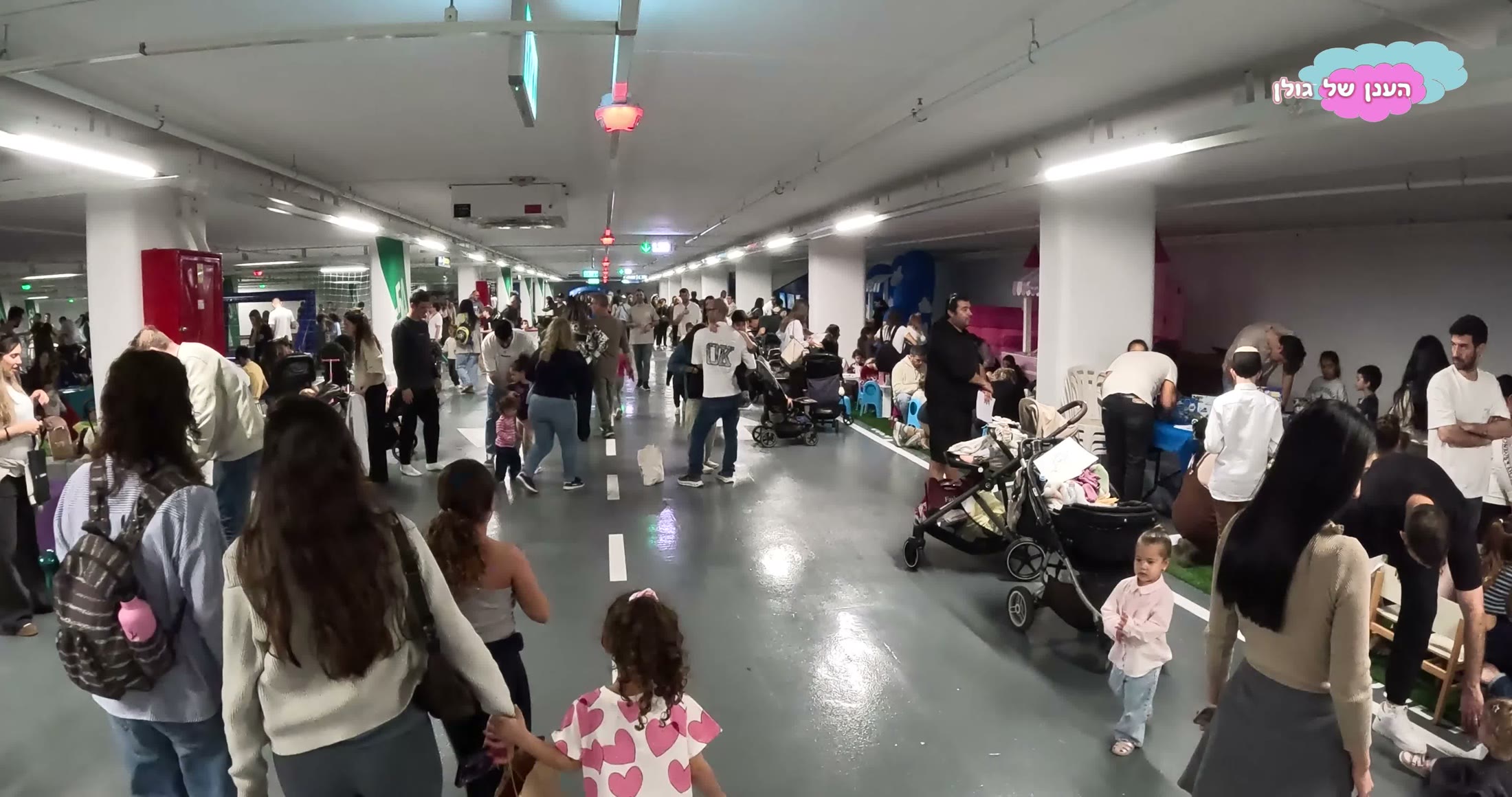 קהל רב וצפוף של משפחות בתוך ה-FUN ZONE, עגלות ילדים וטירה ורודה ברקע